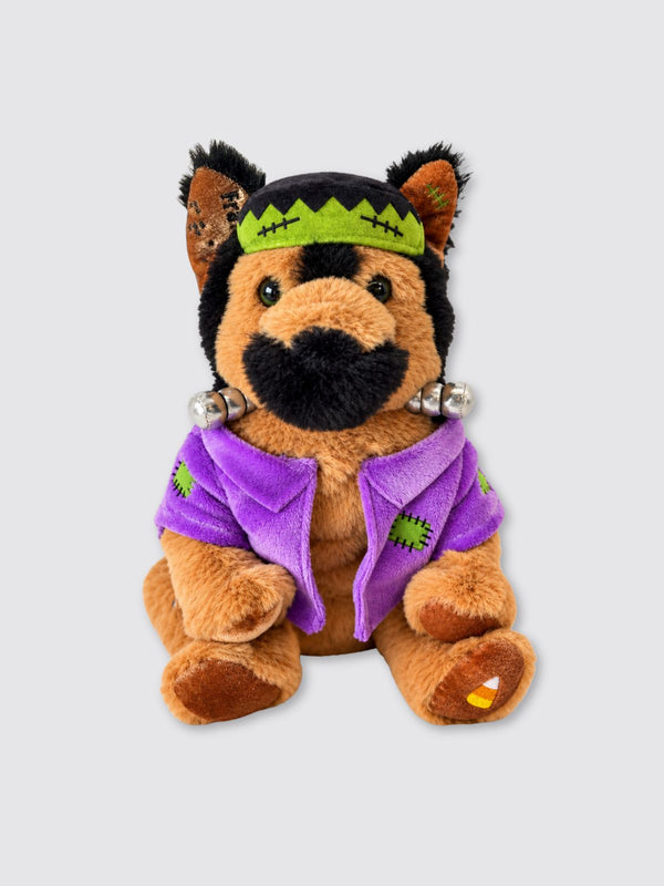 Two Blind Brothers - Guide Dog FRANKY Plush-German-Shepherd-in-a-Frankenstein-costume-with-green-stitched-hat,-neck-bolts,-purple-patched-jacket,-and-candy-corn-on-one-paw.